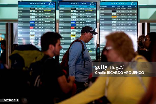 People walk in front of a flight status monitor at the Luis Munoz Marin international airport in San Juan, Puerto Rico on March 14, 2020.