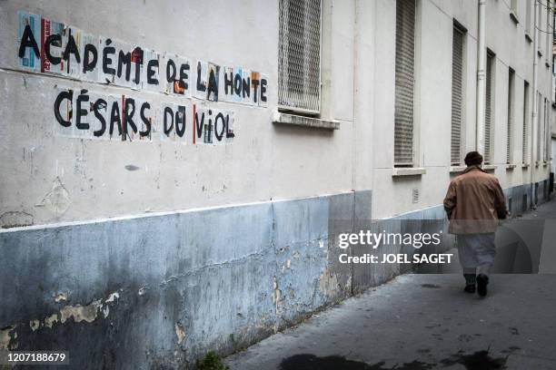 Pedestrian walks past posters reading "Academy of shame, Cesars of rape" against the Cesar Academy which holds the Cesar Film Awards and who gave the...