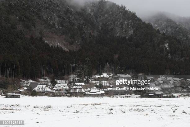 tranquil winter landscape with snow covered traditional japanese thatched roof houses and farm field after snowfall in cloudy overcast day.fog lies over the mountains covered with cedar trees. miyama kayabuki-no-sato village ,kyoto prefecture,japan - kyoto covered with first snow of the season imagens e fotografias de stock