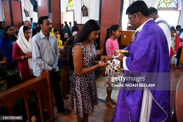 Catholic devotees receive Holy communion on their hands from a priest amid concerns of the spread of the COVID-19 coronavirus during a mass at Saint...