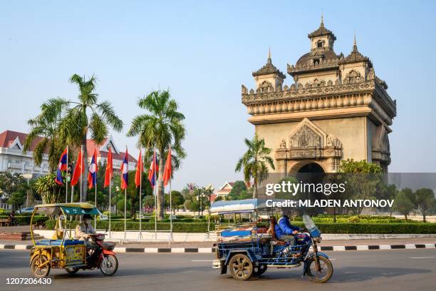 This photograph taken on March 12, 2020 shows traditional tuk tuks passing in front of the Patuxai war monument in the centre of Vientiane.