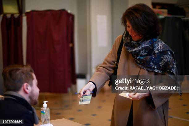 Paris mayoral candidate Agnes Buzyn shows her identity card to an official before voting during the first round of municipal elections in Paris on...