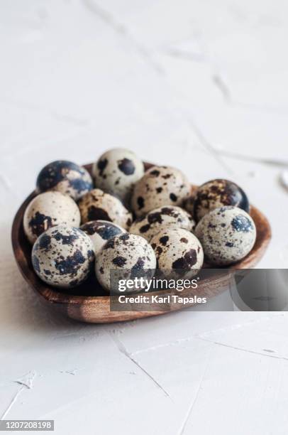 quail eggs in a heart shaped bowl on a wooden white table - uovo di quaglia foto e immagini stock