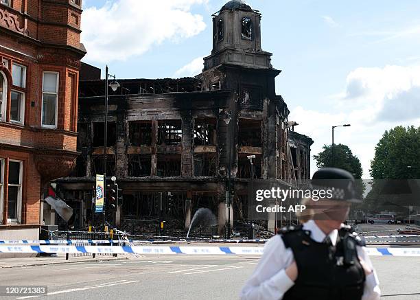 Police officer stands guard August 8 outside the fire damaged Carpetright shop on Tottenham High Road, following disturbances on Saturday night....
