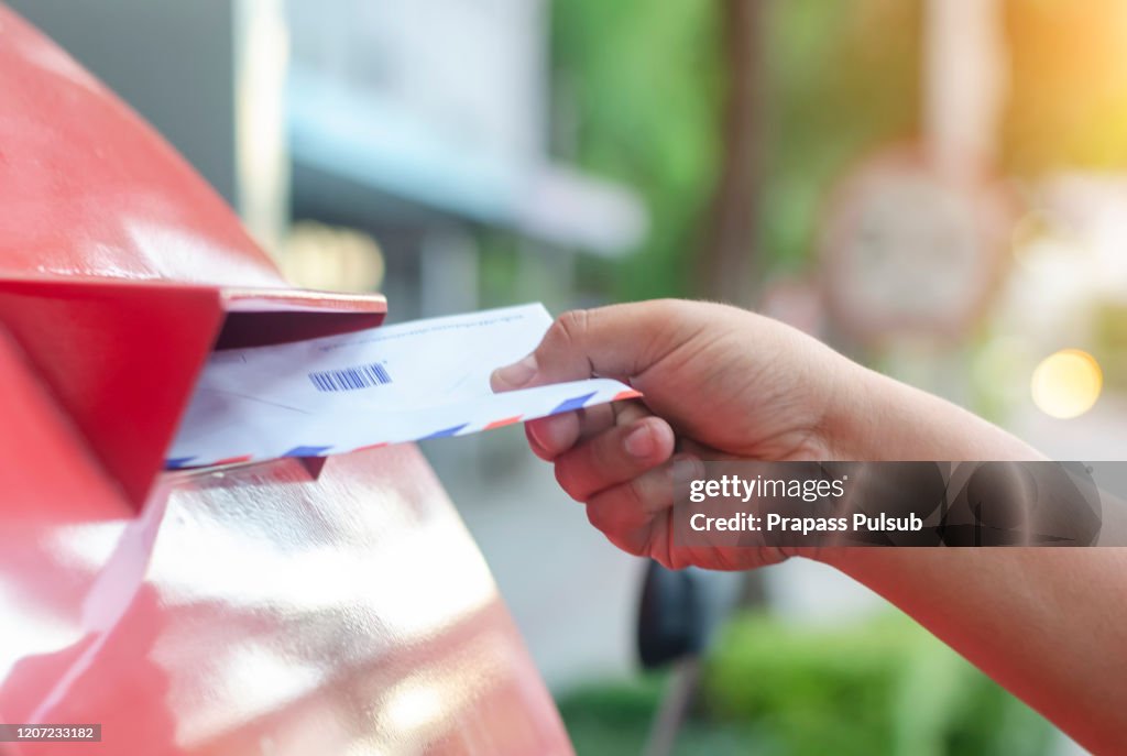 Posting a letter to red british postbox on street