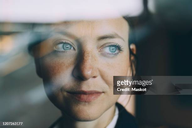 thoughtful female executive looking away seen through glass at workplace - fantasie stockfoto's en -beelden