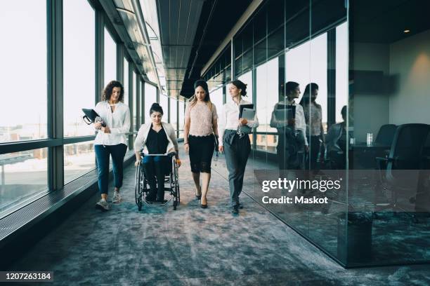 businesswomen walking with disabled female entrepreneur in corridor at workplace - differing abilities female business stock-fotos und bilder