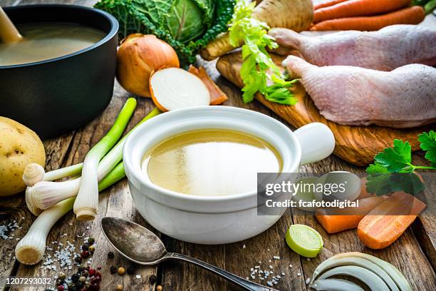 caldo de pollo en un tazón e ingredientes en la mesa de cocina de madera - sopa images fotografías e imágenes de stock