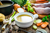 Chicken bouillon in a bowl and ingredients on wooden kitchen table