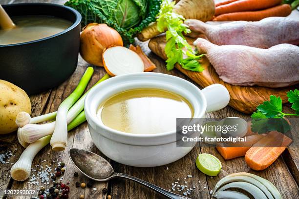 chicken bouillon in a bowl and ingredients on wooden kitchen table - sopa imagens e fotografias de stock