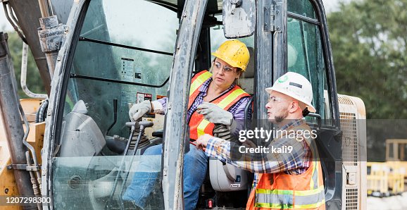 Two multi-ethnic construction workers with earth mover Two multi-ethnic construction workers with earth mover