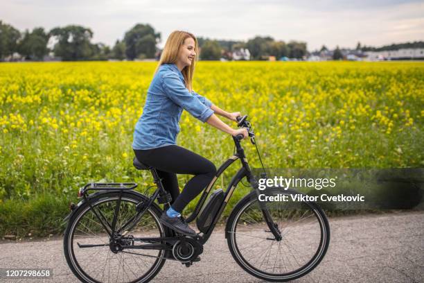 happy young woman riding on her electric bicycle - ebike stock pictures, royalty-free photos & images