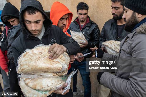 Displaced Syrian man carries a bag of bread as people wait in a queue as an NGO delivers bread in a stadium which has been turned into a makeshift...