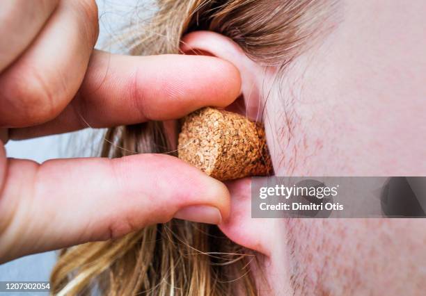 closeup of hand plugging ear with cork - bouchon en liège photos et images de collection
