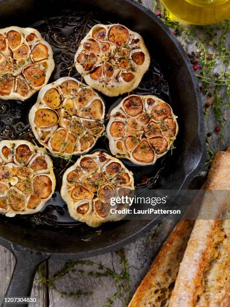 ajo asado con sal, pimienta, tomillo y aceite de oliva en una sartén de hierro fundido - ajo fotografías e imágenes de stock