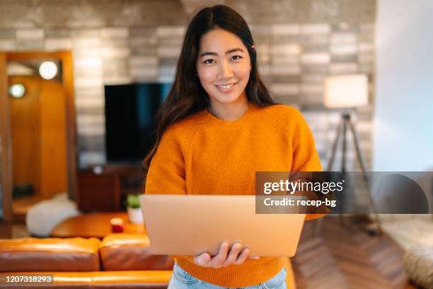 young woman holding laptop and smiling for camera - standing with laptop imagens e fotografias de stock