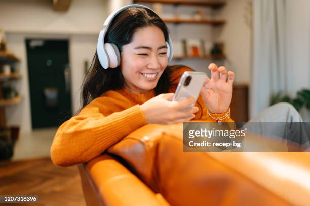 stylish young woman listening to music at home - asian females on a phone imagens e fotografias de stock