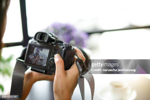 young woman photographer looking at camera screen sitting at the table with cup of coffee. concept of occupation and lifestyle. - executive editor stockfoto's en -beelden