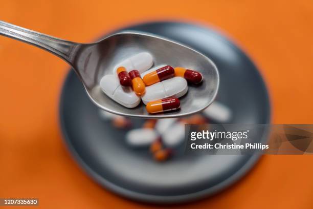 a spoon full of medicine (pills and capsules) above a plate filled with pills and capsules. - resisent tegen antibiotica stockfoto's en -beelden