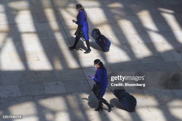 Airline crew members wear protective masks as they wheel trolley cases through the departures terminal at Madrid Barajas airport, operated by Aena...