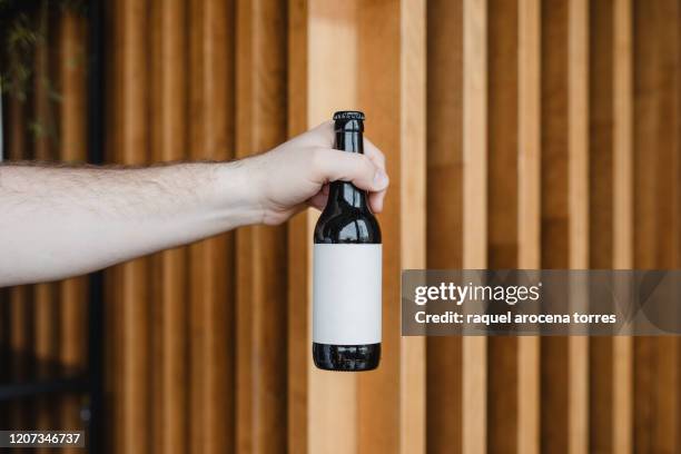 hand holding a beer bottle - bierflaschen stock-fotos und bilder