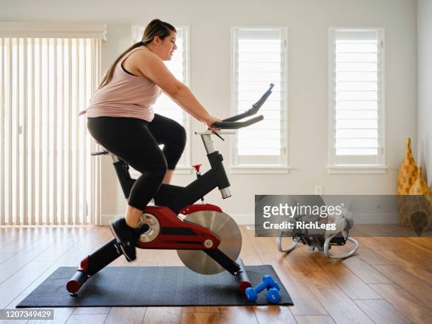 madre joven usando la bicicleta de ejercicio en un hogar - exercise bike fotografías e imágenes de stock