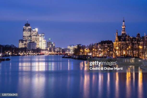 dawn over the amstel river where traditional dutch architecture contrasts with modern office building in amsterdam, netherlands - amsterdam sunrise stockfoto's en -beelden