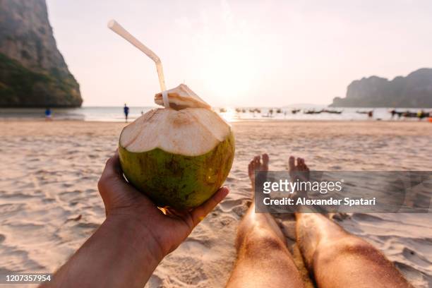 man drinking coconut from personal perspective at the beach at sunset - beach holiday stock-fotos und bilder