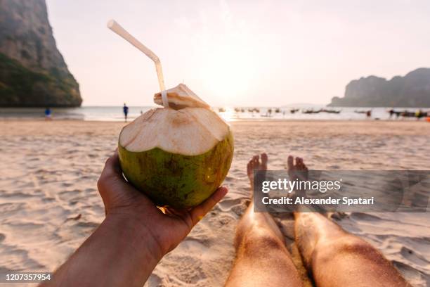 man drinking coconut from personal perspective at the beach at sunset - acqua di cocco foto e immagini stock