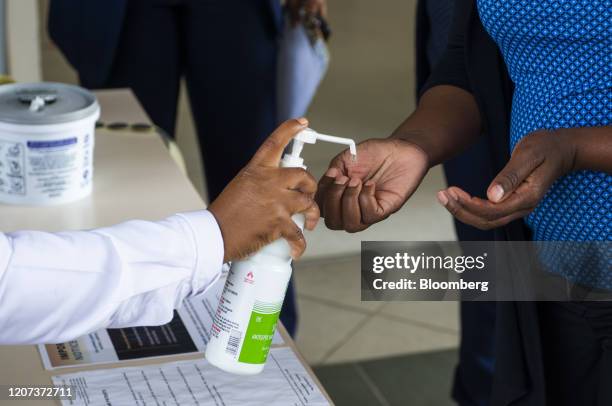 Healthcare worker pumps sanitizing hand gel onto the hands of a visitor at a health screening desk outside the entrance to Netcare Pretoria East...