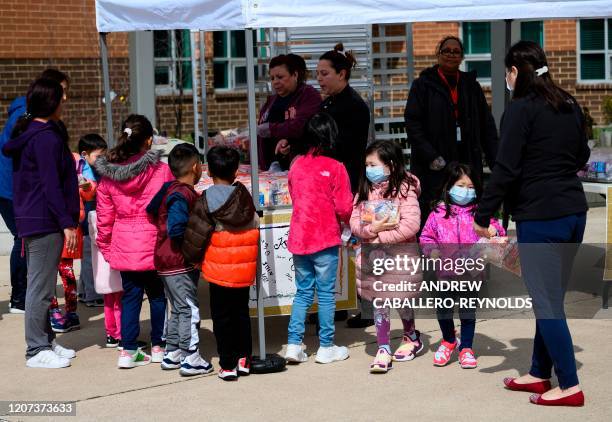 Children, some wearing face masks as a preventive measure, pick up free lunch at Kenmore Middle School in Arlington, Virginia on March 16 after...