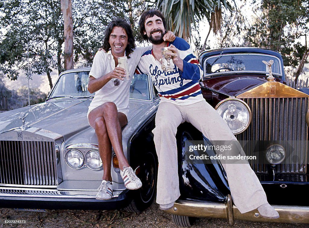 Singer Alice Cooper And His Friend, Keith Moon, The Who's Celebrated Drummer Sitting On the Hoods Of Their Rolls-Royce Cars On Mulholland Drive In The Hollywood Hills In Los Angeles, California, June 1976.