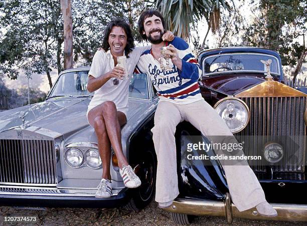 Singer, songwriter and actor Alice Cooper with his friend Keith Moon, the legendary drummer for The Who, share a cocktail on the hoods of their...