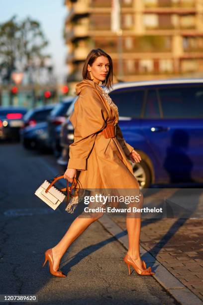 Landiana Cerciu wears a brown long coat with mesh, a dress, a large leather belt, pointy shoes, a white bag, outside Alberta Ferretti, during Milan...