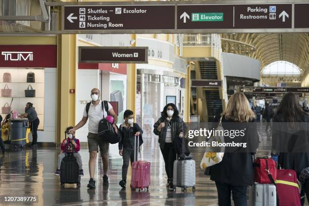 Family wear protective face masks while carrying luggage at the Ronald Reagan National Airport in Arlington, Virginia, U.S., on Monday, March 16,...