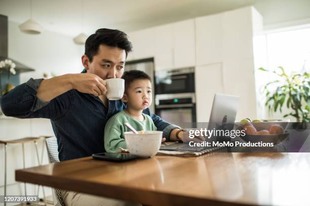 father multi-tasking with young son (2 yrs) at kitchen table - père célibataire photos et images de collection