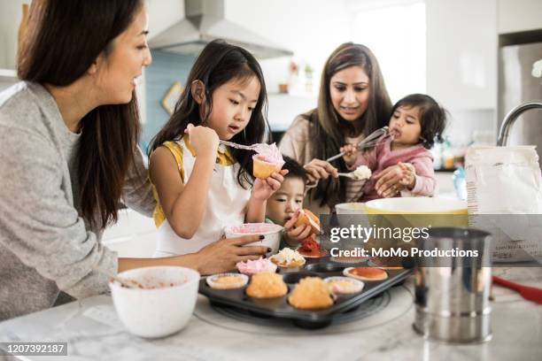 2 mothers with children makings cupcakes in kitchen - boy cooking stock pictures, royalty-free photos & images