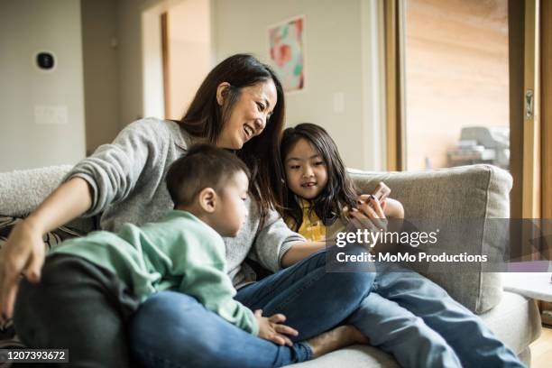 mother using mobile device with young children on couch - family with two children stock pictures, royalty-free photos & images