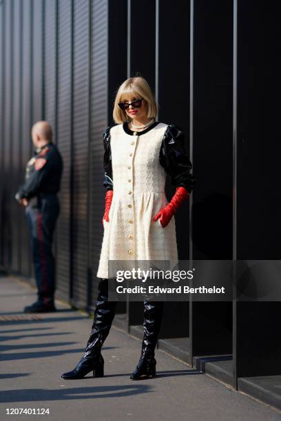 Xenia Adonts wears sunglasses, a white tweed dress with black shiny puff sleeves, a necklace, black shiny pvc thigh high boots, red gloves, outside...