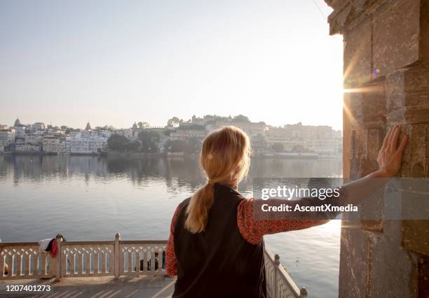 reife frau erkundet einen ghat bei sonnenaufgang, blickt über den see - udaipur palace stock-fotos und bilder
