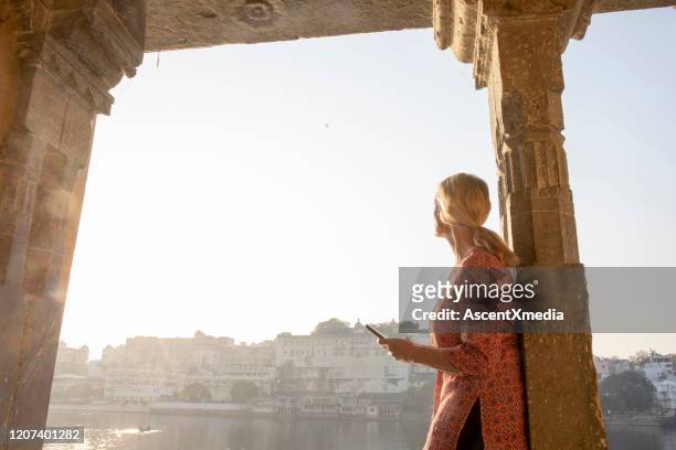 reife frau erkundet einen ghat bei sonnenaufgang, blickt über den see - rajasthani women stock-fotos und bilder