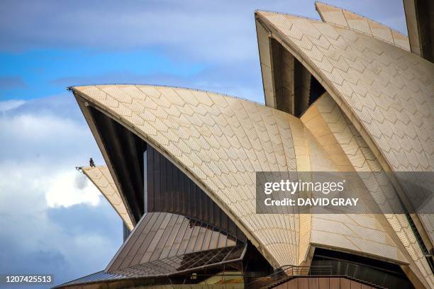 Worker stands atop of the roof of the Sydney Opera House in Sydney on March 17, 2020. - Management of the iconic building on March 17 announced the...