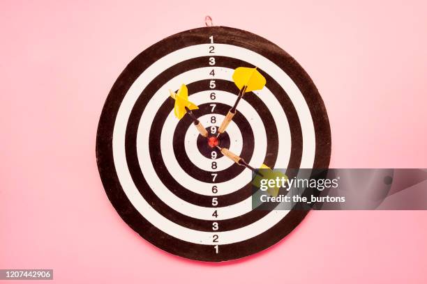 high angle view of a dartboard and three yellow darts on pink colored background - darttavla bildbanksfoton och bilder