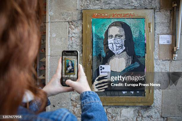Woman makes a photo with her mobile next to the paint of a Mona Lisa with a mobile phone and a mask, work of the graffiti artist TV Boy, called...
