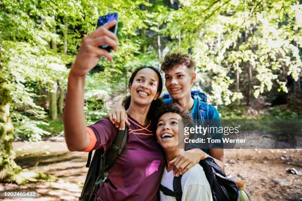 mother talking selfie h two sons while hiking - boy taking picture in forest stock-fotos und bilder