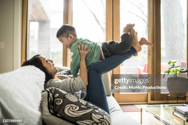 mother playing with young son (2 yrs) on couch at home - love connection family stockfoto's en -beelden