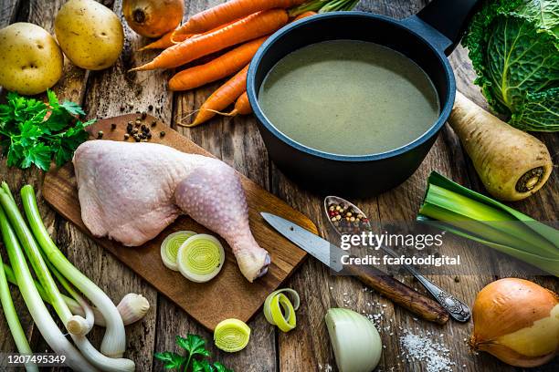 hühnerbouillon in einer kochpfanne mit zutaten auf holzküchentisch - hühnerbrühe stock-fotos und bilder