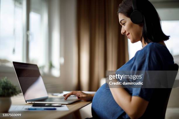 zwangere vrouw met hoofdtelefoons die laptop gebruiken - pregnancy class stockfoto's en -beelden