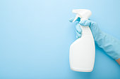 Hand in rubber protective glove holding white spray bottle. Detergent for different surfaces in kitchen, bathroom and other rooms. Closeup. Empty place for text or logo. Light pastel blue background.