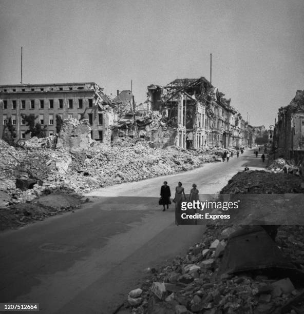 Three women walk along bombed damaged streets and buildings showing the destruction of the city in July 1945 following the allied occupation of...
